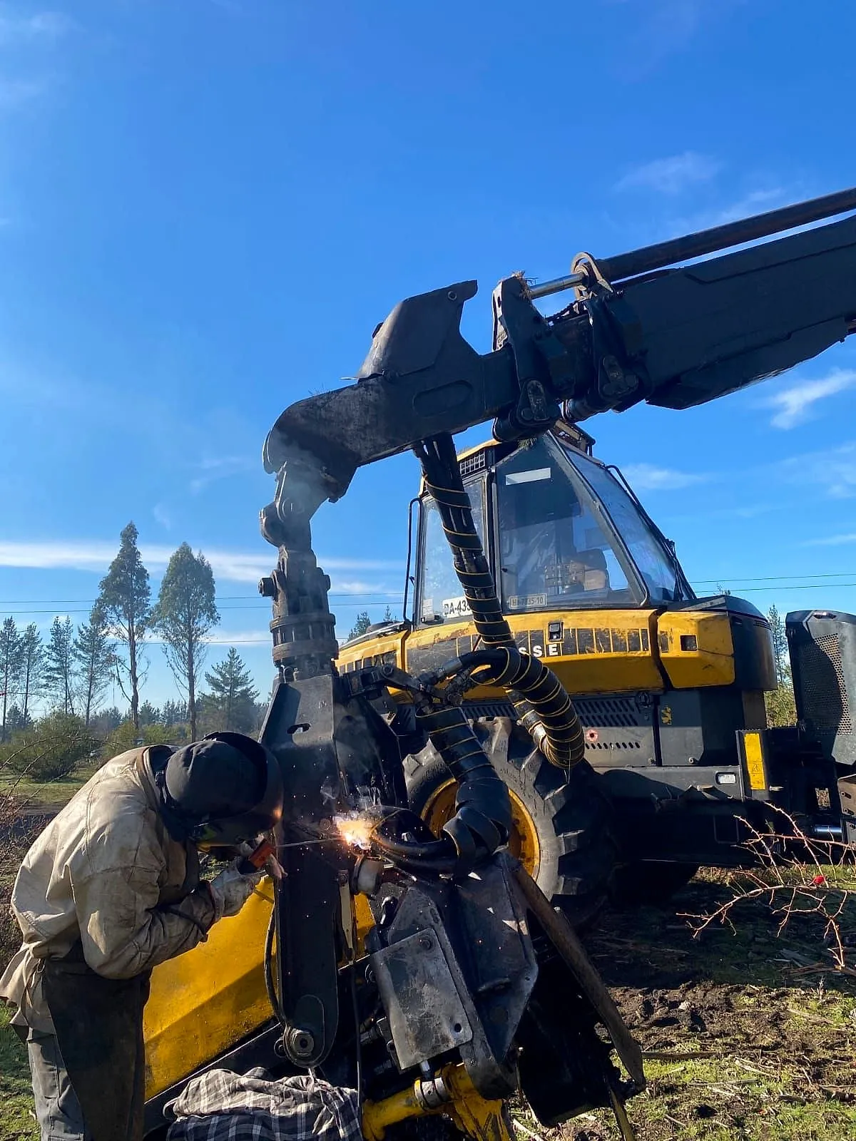 Soldador trabajando en terreno sobre una máquina forestal