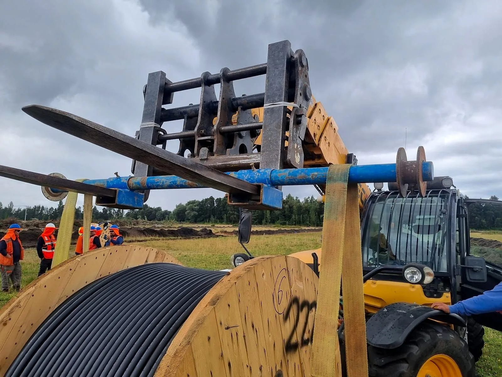 Manipulador telescópico moviendo un carrete de cable en terreno